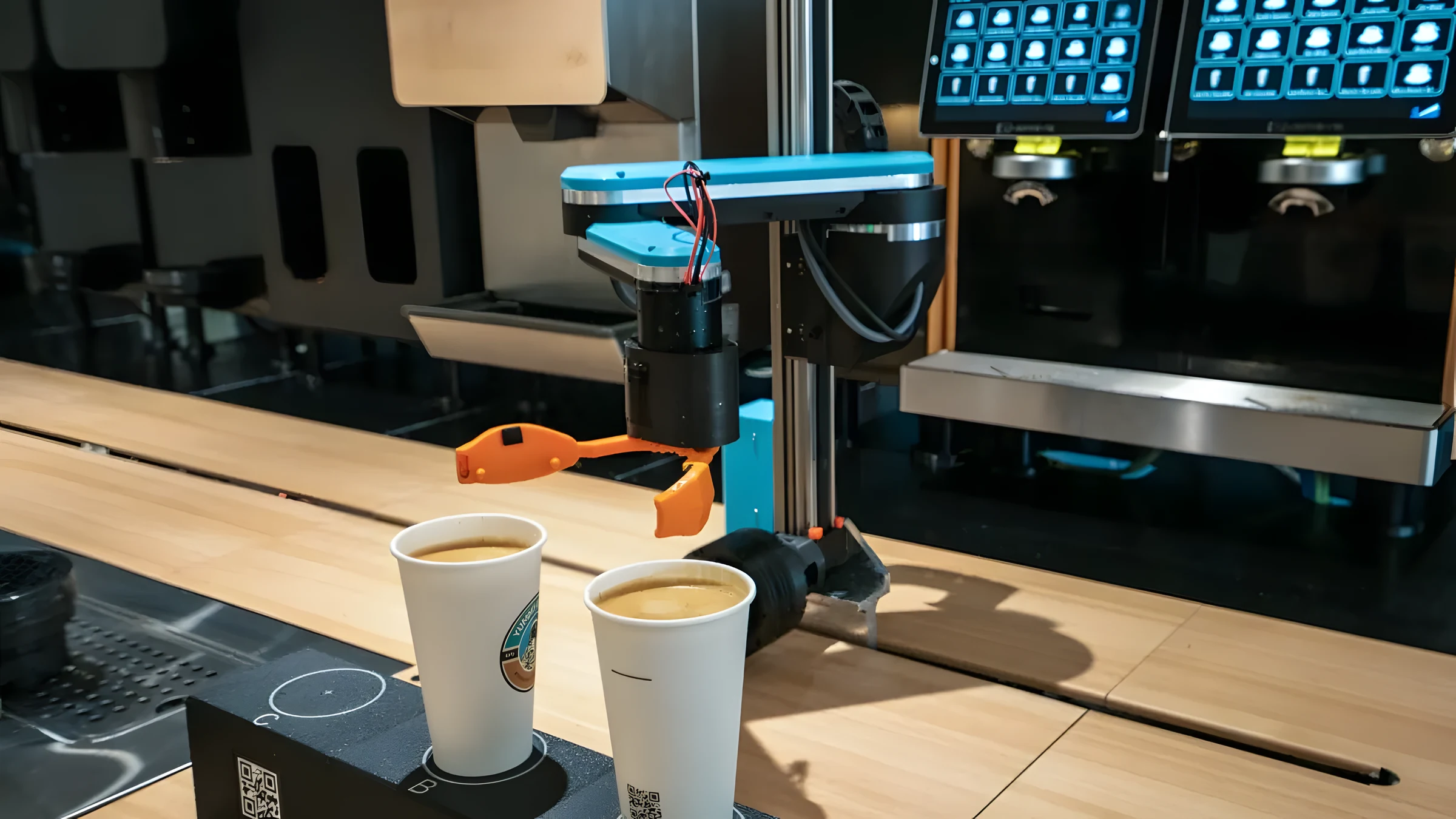 Robotic arm with an orange gripper positioning two cups under the espresso heads