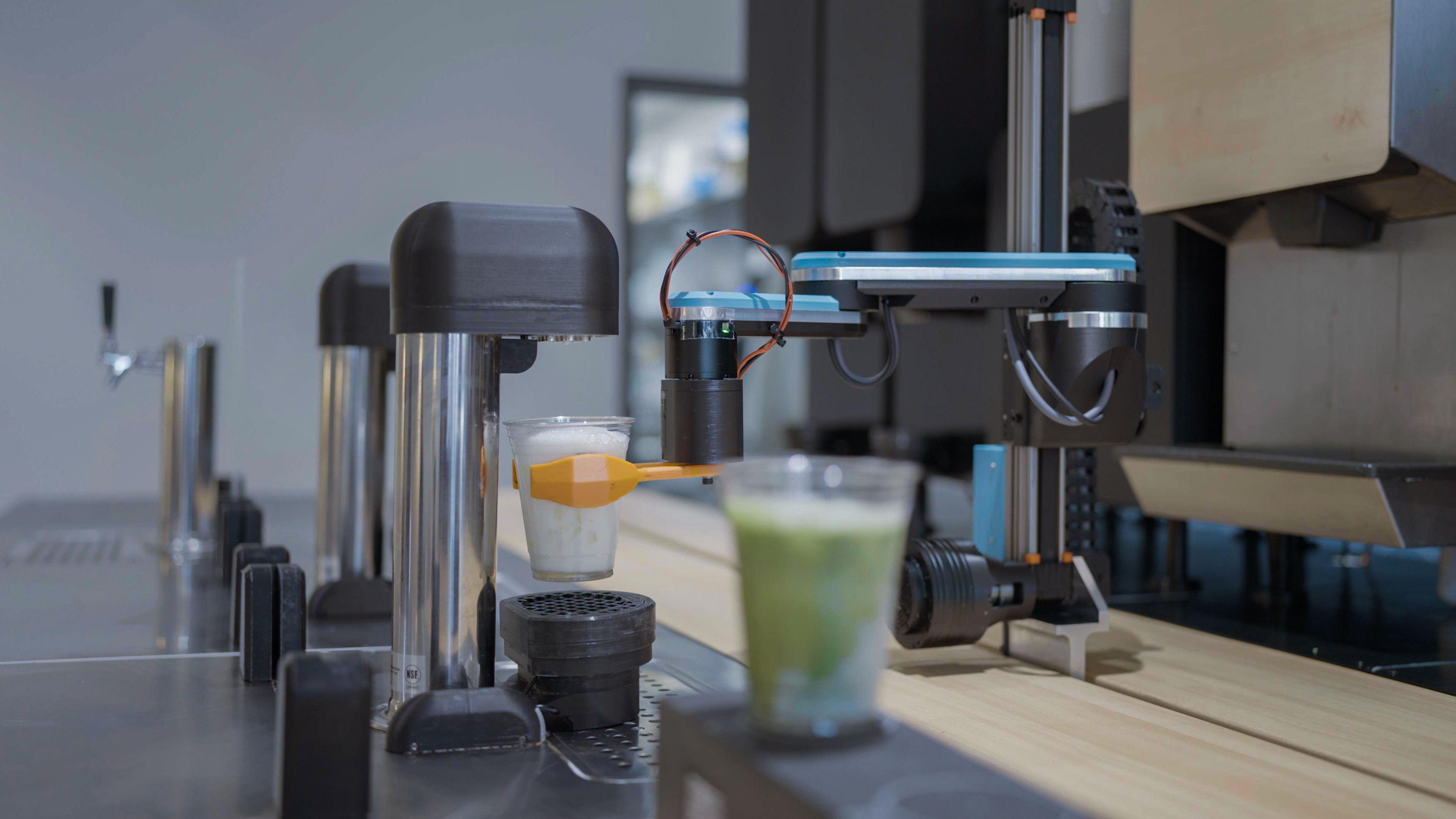The robot arm holding a cup under the dosing station
